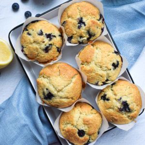 Overhead view of blueberry lemon muffins in a white tin, on a white background with a blue napkin next to it.