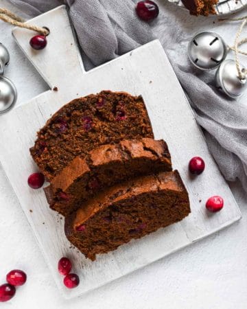 Overhead view of cranberry gingerbread loaf on a grey cutting board and scattered cranberries.