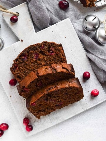 Overhead view of cranberry gingerbread loaf on a grey cutting board and scattered cranberries.
