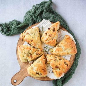 Overhead view of apricot and rosemary scones on a round cutting board with a green linen.