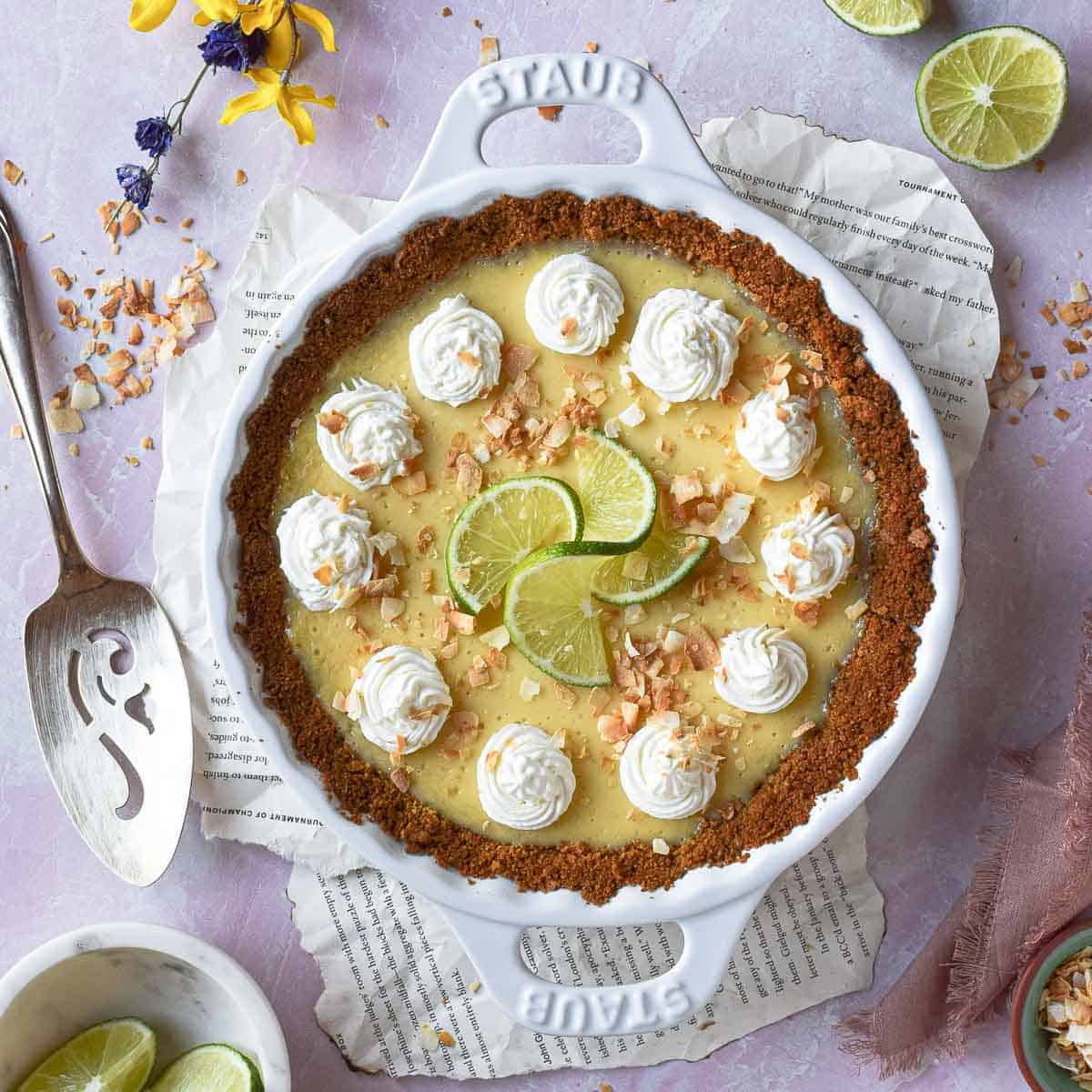 Overhead of a coconut key lime pie in a white pie pan on a pink surface.