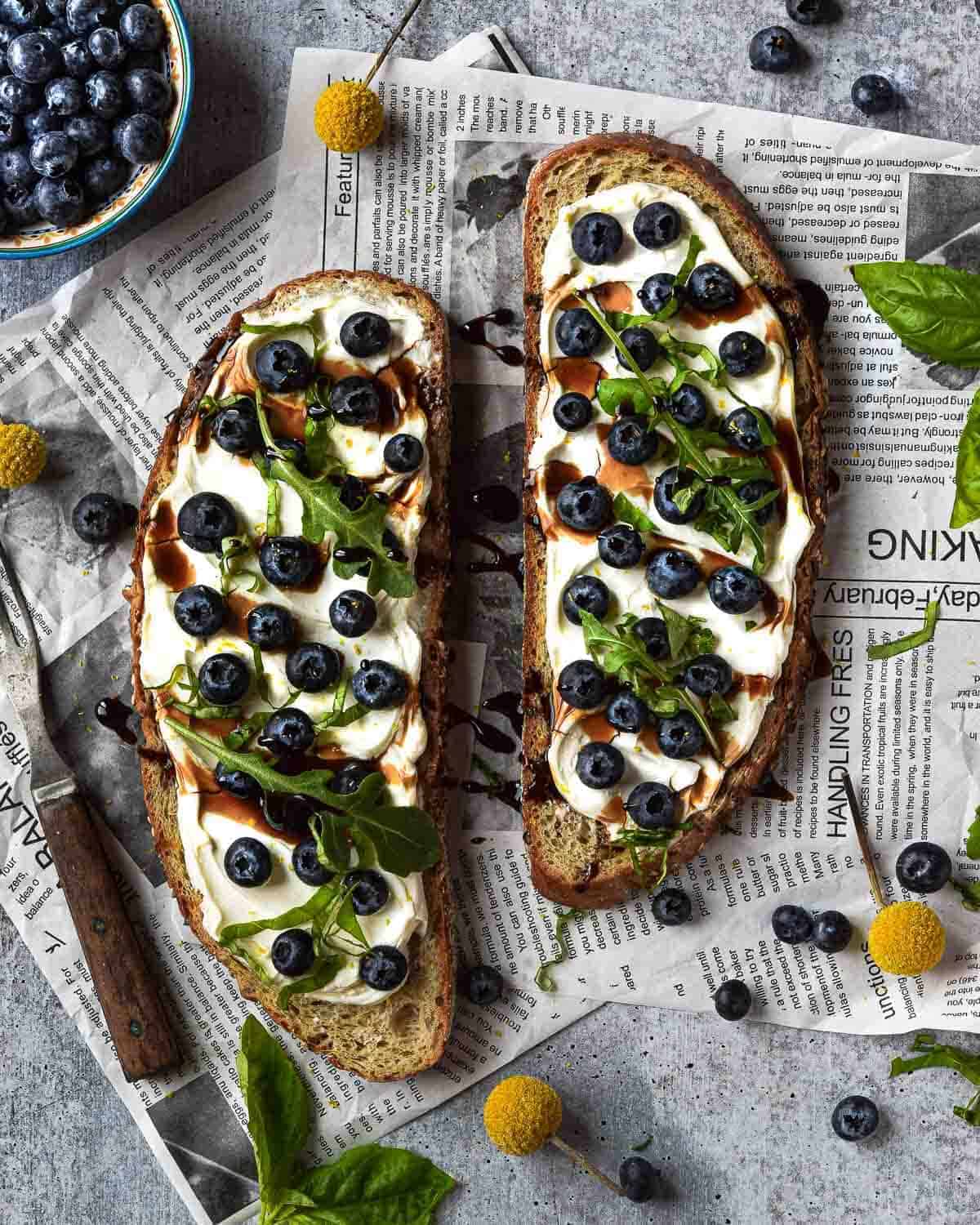 Overhead picture of blueberry toast on newspaper with scattered basil.