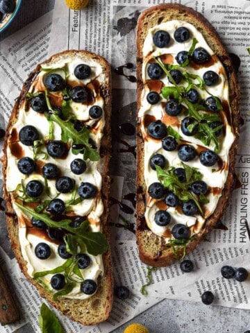 Overhead view of blueberry toast on newspaper with yellow flowers around it