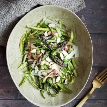 Overhead picture of shaved asparagus salad in a green bowl on a wooden background