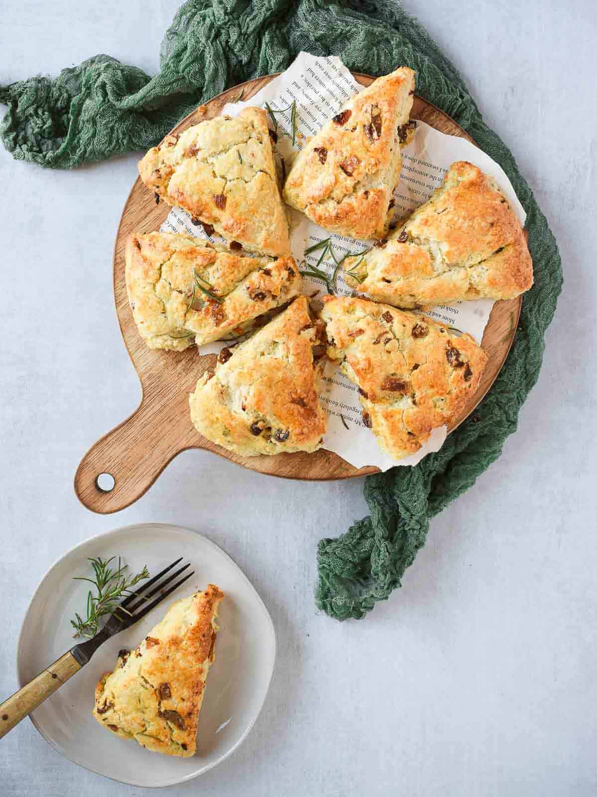 Overhead view of apricot and rosemary scones on a round cutting board and green linen beside it.