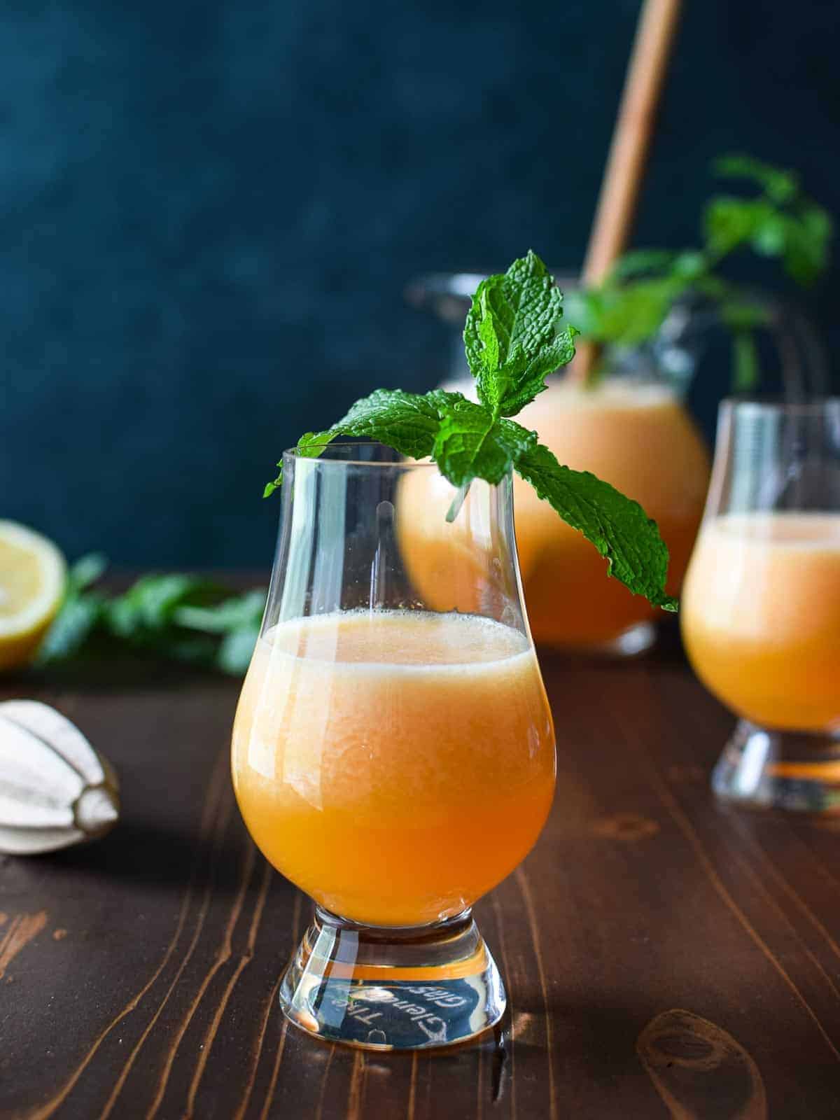 eye-level view of cantaloupe lime agua fresca in a clear glass on a brown table with mint and lime.