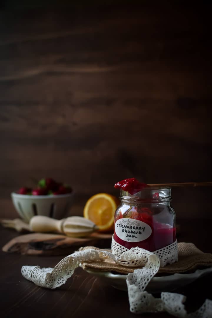 Eye level view of strawberry rhubarb jam on a brown background with strawberries in the background.