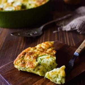Angled view of zucchini pie on a brown cutting board with a fork cut into a slice.
