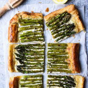 Overhead of asparagus and whipped goat cheese puff pastry tart cut into six pieces with a lemon to the side