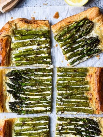 Overhead of asparagus and whipped goat cheese puff pastry tart cut into six pieces with a lemon to the side
