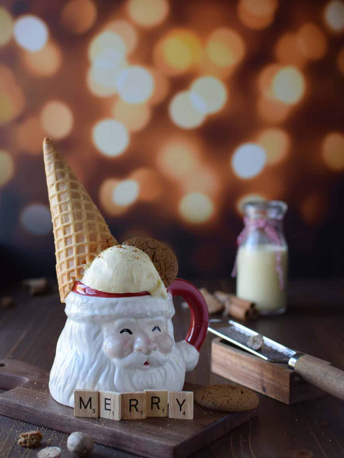 Eye level view of egg nog ice cream in a santa claus mug with a cone on it's head on brown surface with glittery background
