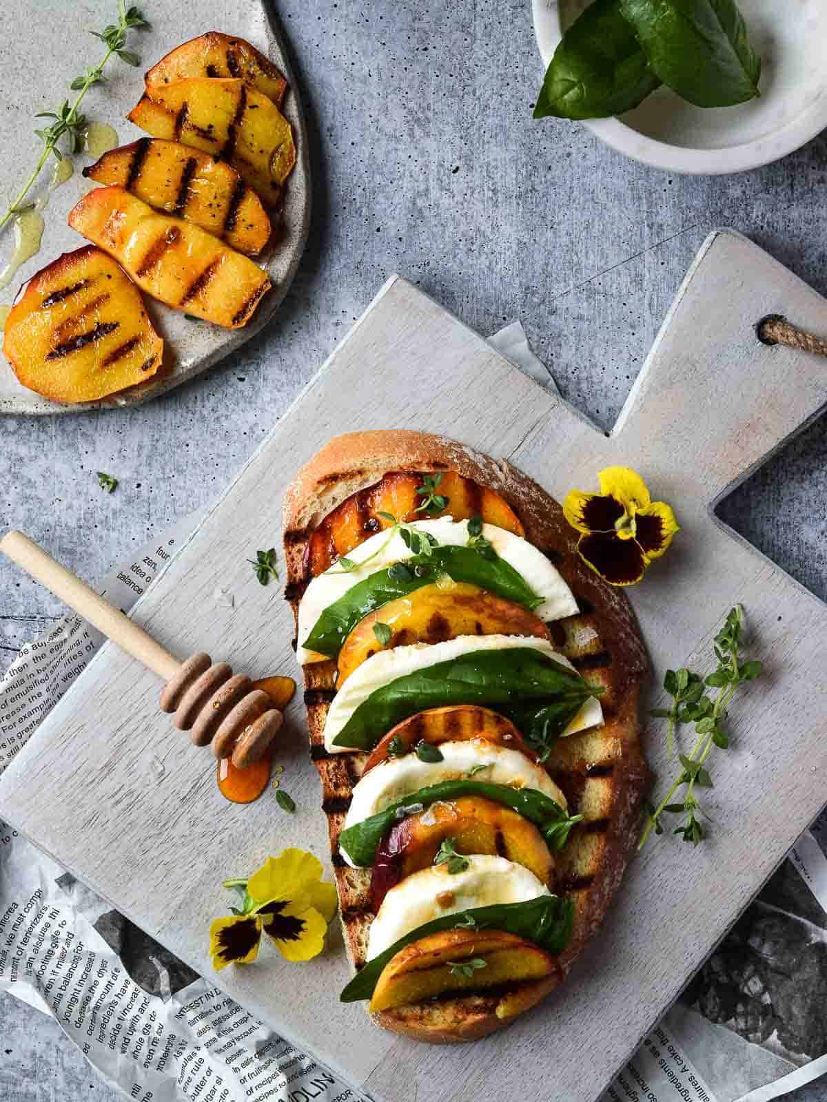 Overhead view of toast with grilled peaches on it layered with mozzerella, basil and balsamic vinegar on a grey cutting board