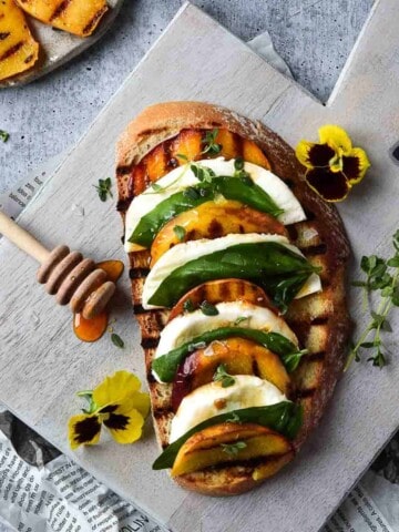 Overhead view of toast with grilled peaches on it layered with mozzerella, basil and balsamic vinegar on a grey cutting board
