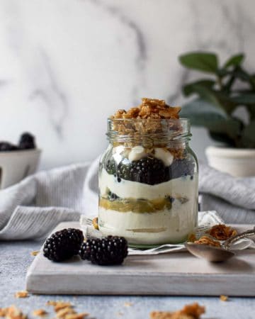 Eye level view of parfait in a jar layered with yogurt, blackberries lemon curd and granola on a grey background.
