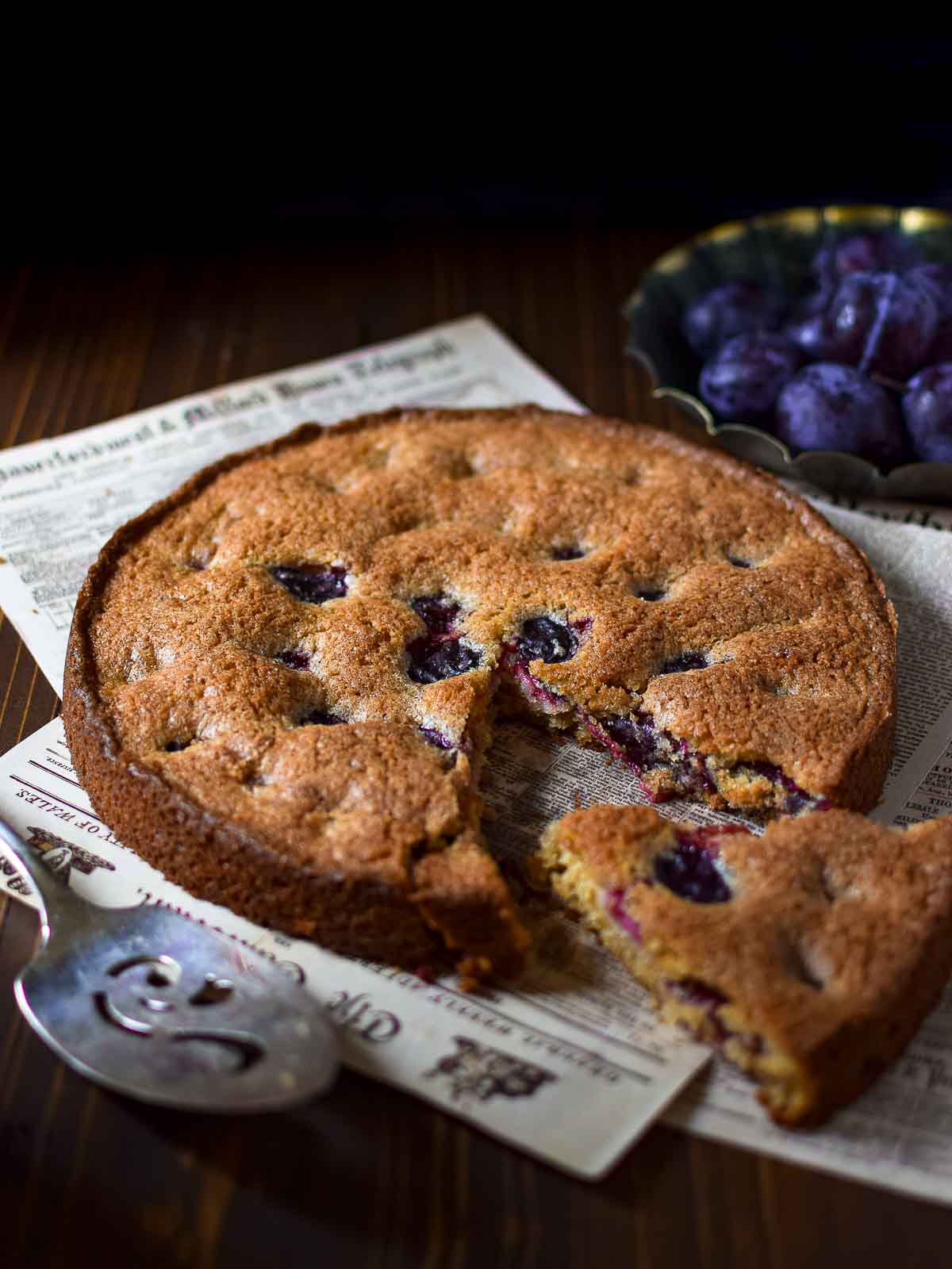 Angled view of plum cake with a slice removed on a wood surface.