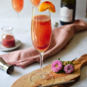 View of plum bellini on a cutting board with a bottle of prosecco in the background.