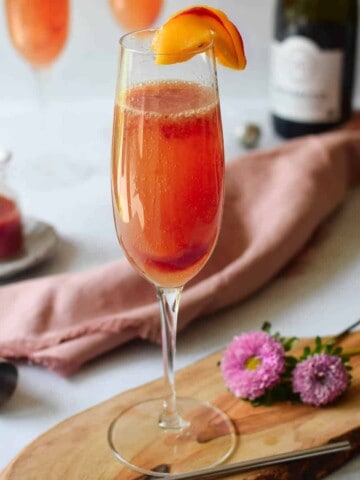 View of plum bellini on a cutting board with a bottle of prosecco in the background.