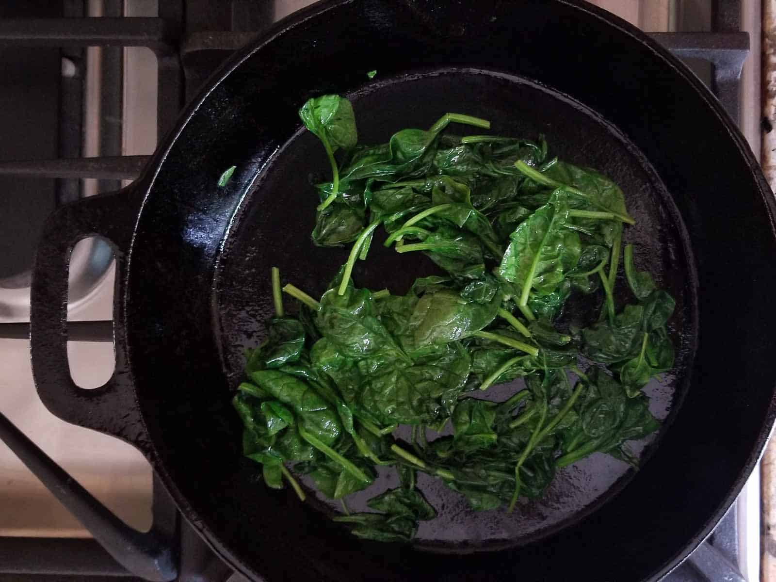 Process shot of cooked spinach in a skillet for a butternut squash frittata.