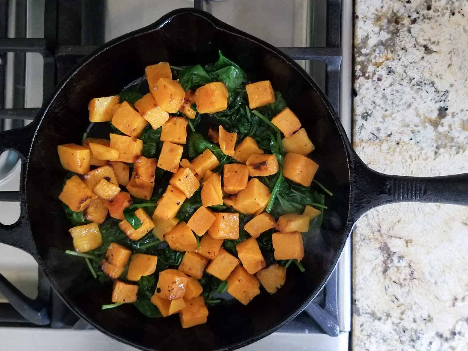 Process shot of wilted spinach and butternut squash cooking in a cast iron skillet.