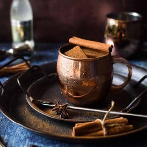 Chai Moscow mule in a copper mug with a cinnamon stick on fire.