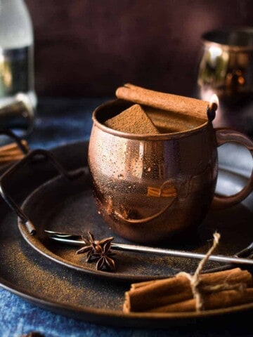 Chai Moscow mule in a copper mug with a cinnamon stick on fire.