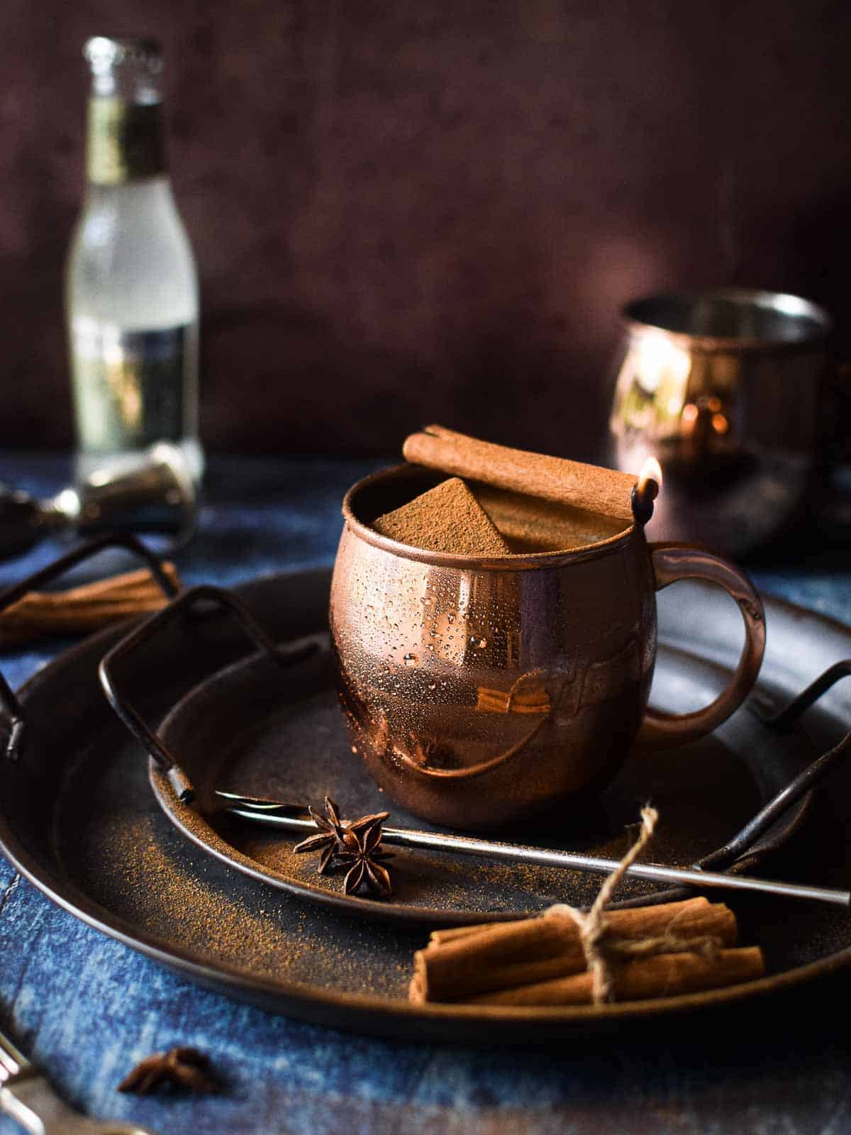 Chai Moscow mule in a copper mug with a cinnamon stick on fire.