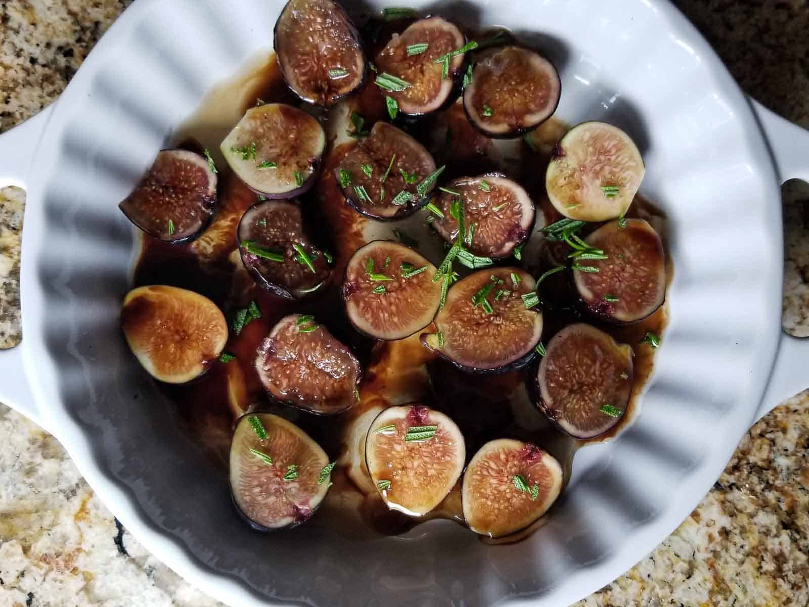 Marinated sliced figs in white bowl with roseamary.