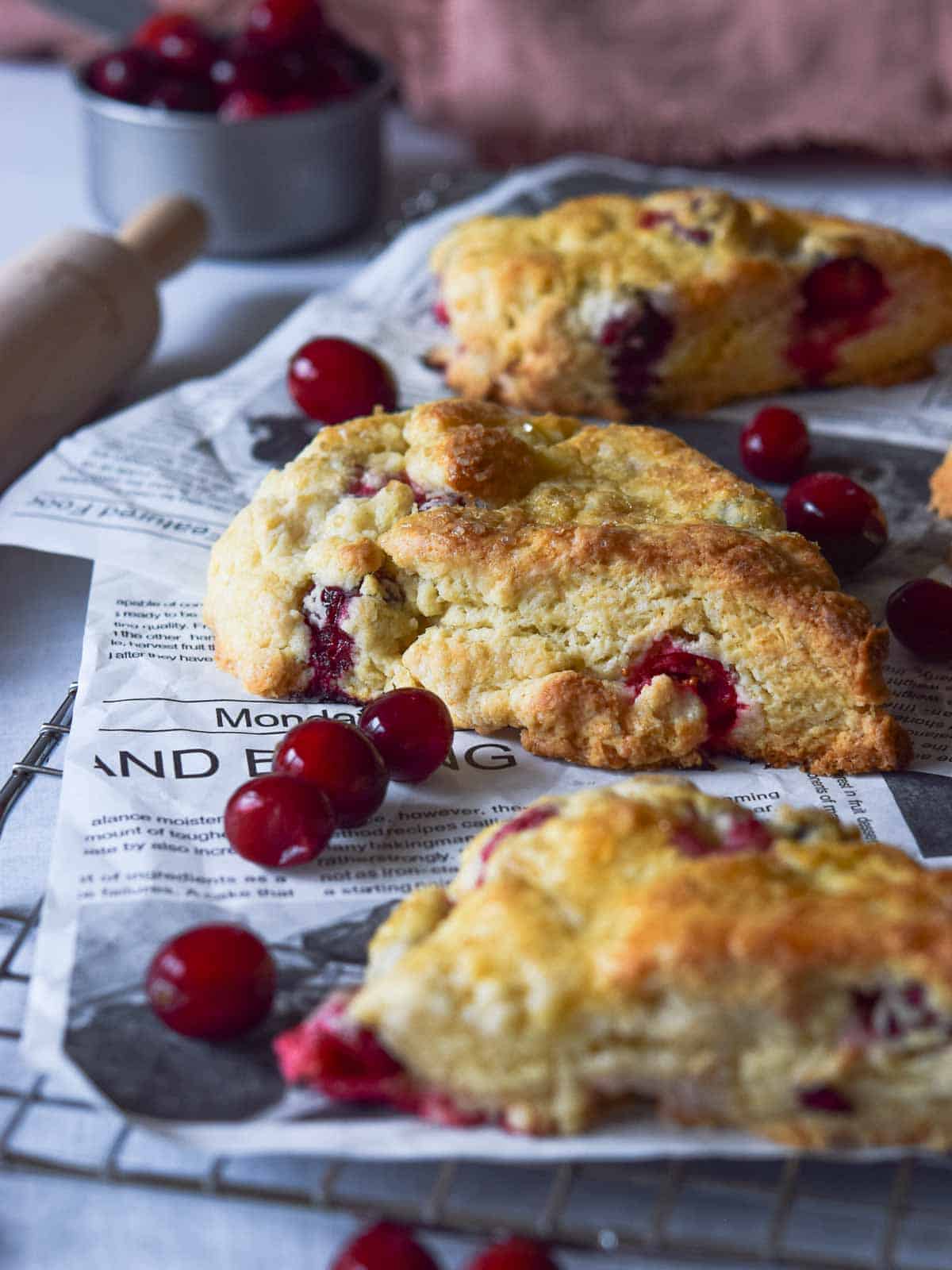 Angled view of cranberry orange scones on a cooling rack with scattered cranberries.