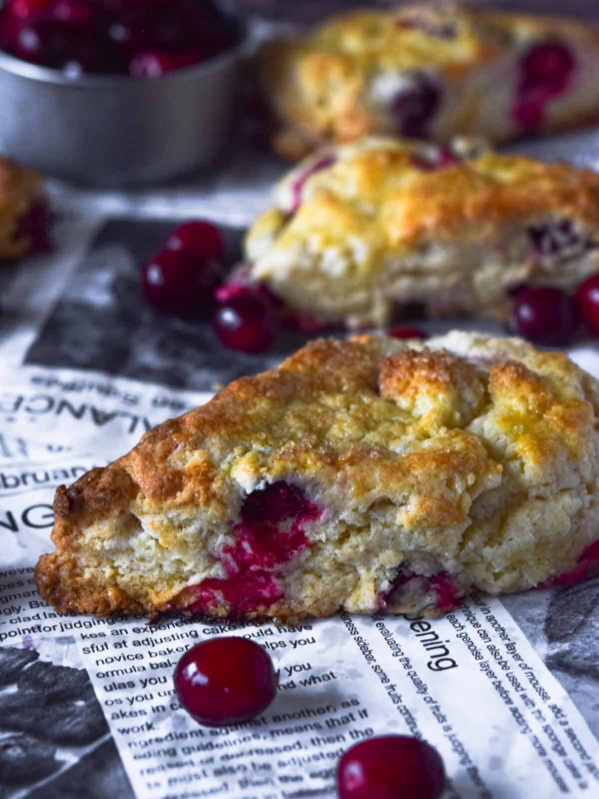 Close up view of cranberry orange scones on parchment paper with scattered cranberries.
