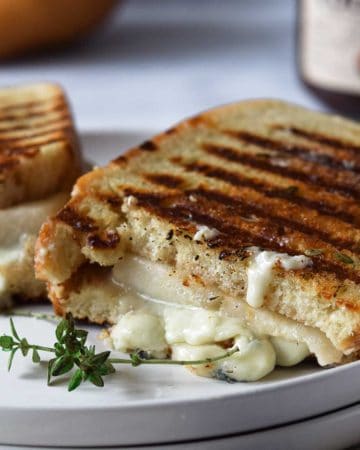 Gorgonzola grilled cheese cut in half on a white plate.