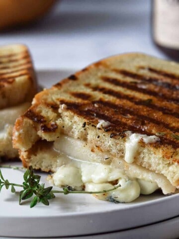 Gorgonzola grilled cheese cut in half on a white plate.