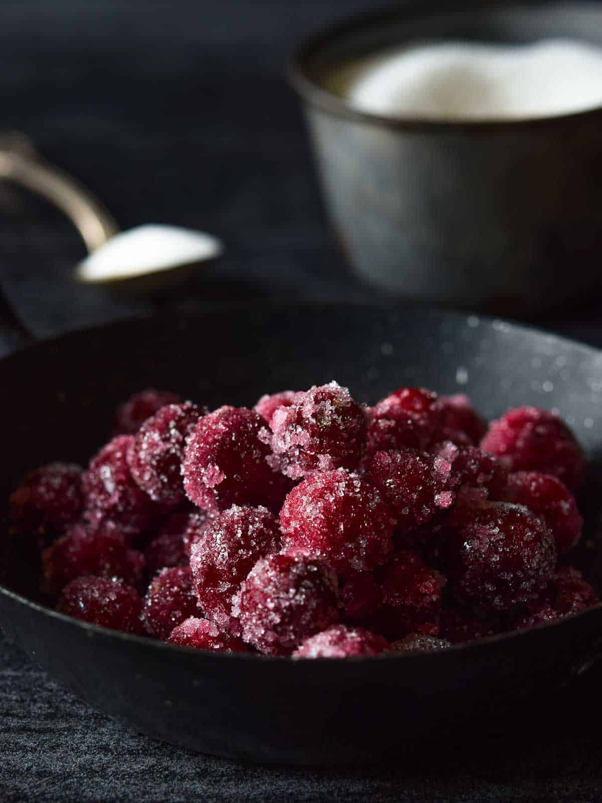 Sugared cranberries in a black bowl.