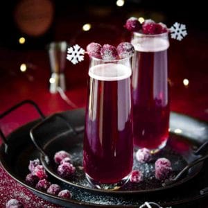 Cranberry mimosas with sugared cranberries on a black tray.