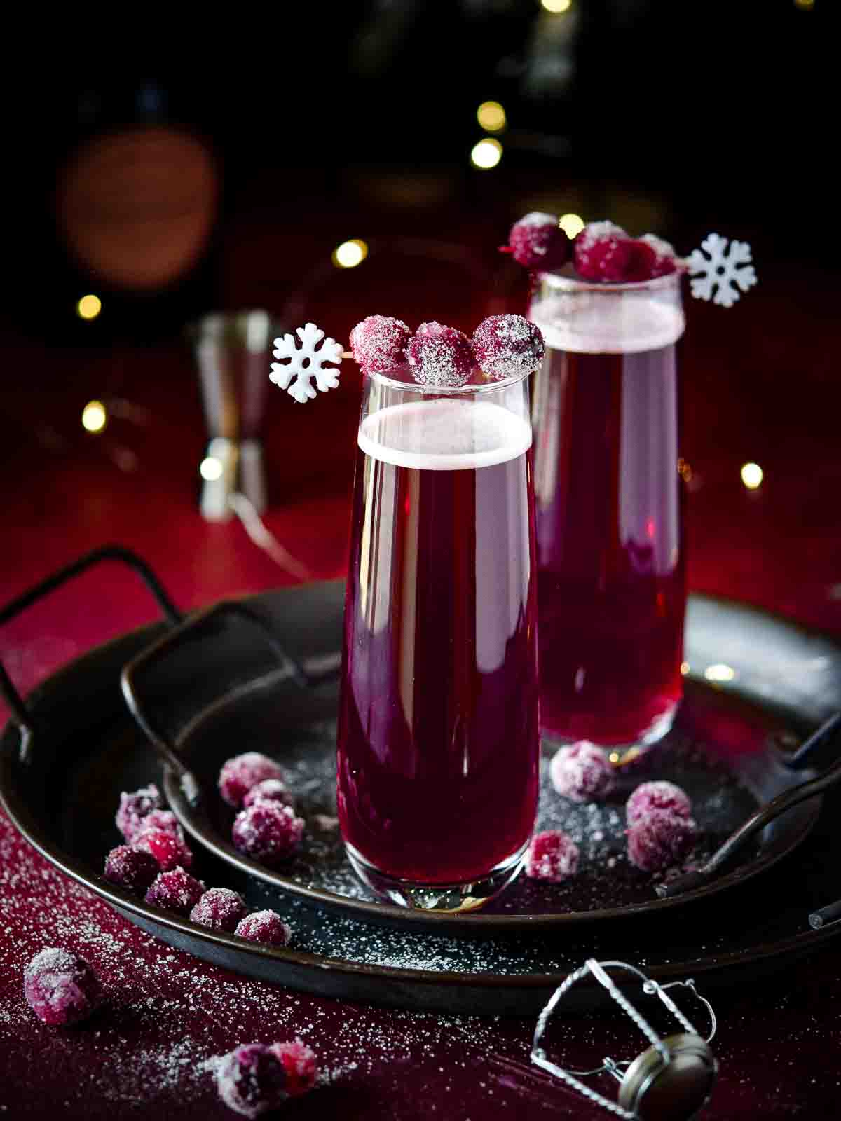 Cranberry mimosas with sugared cranberries on a black tray.