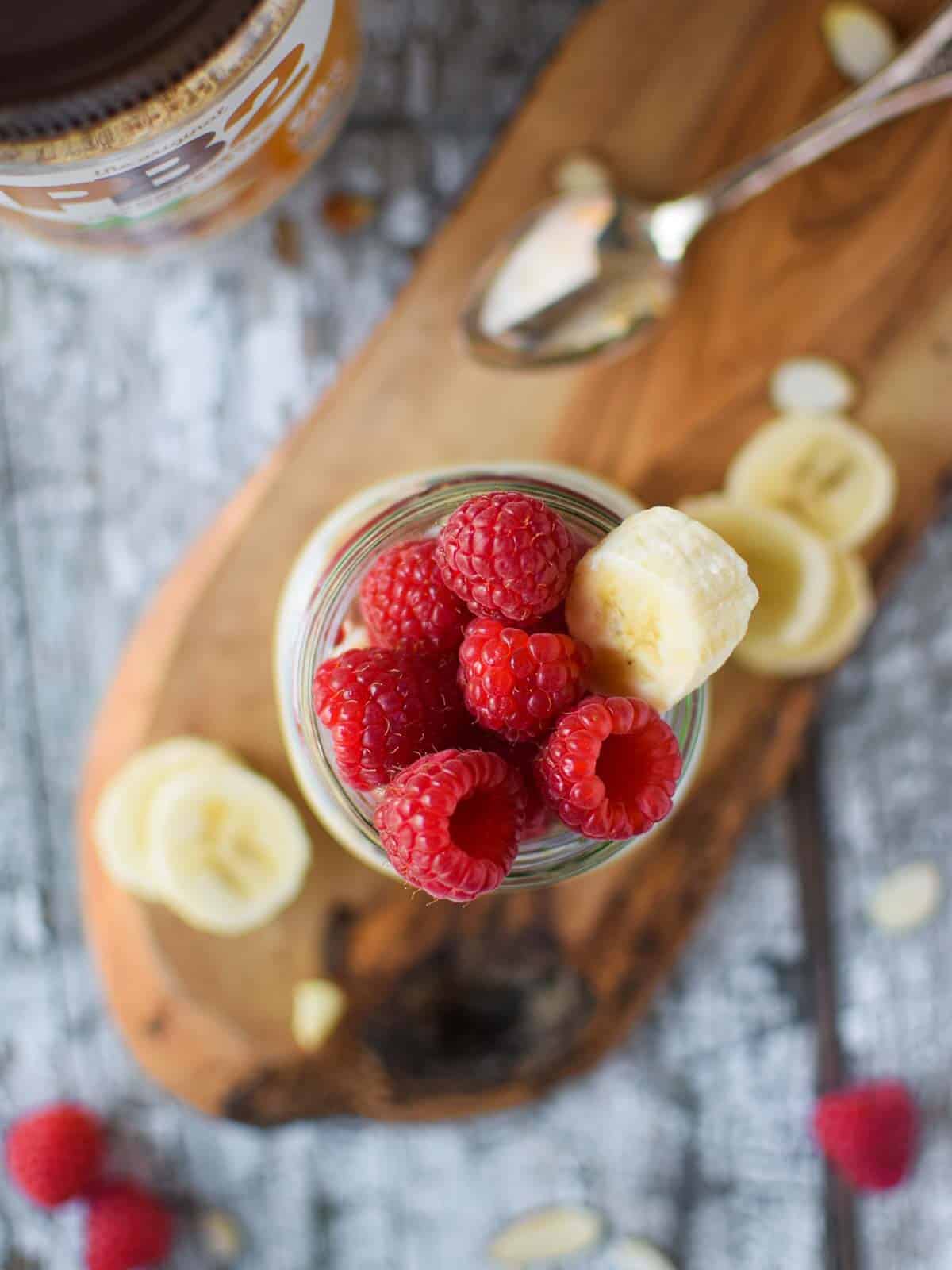 Overhead picture of overnight oats in a jar on a wood service with raspberries on top.