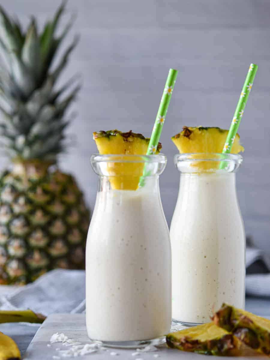 Two banana pineapple smoothies in glasses with a pineapple in the background.