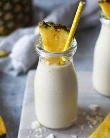 Close-up of banana and pineapple smoothie in a clear glass with a straw.