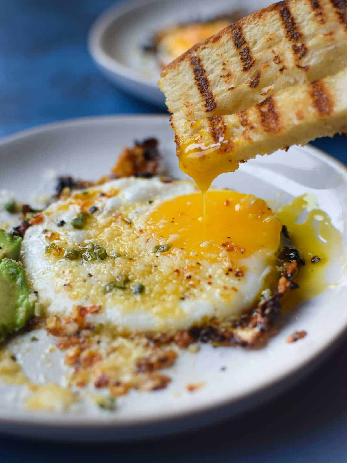 Fried egg with bread being dunked in a runny yolk.