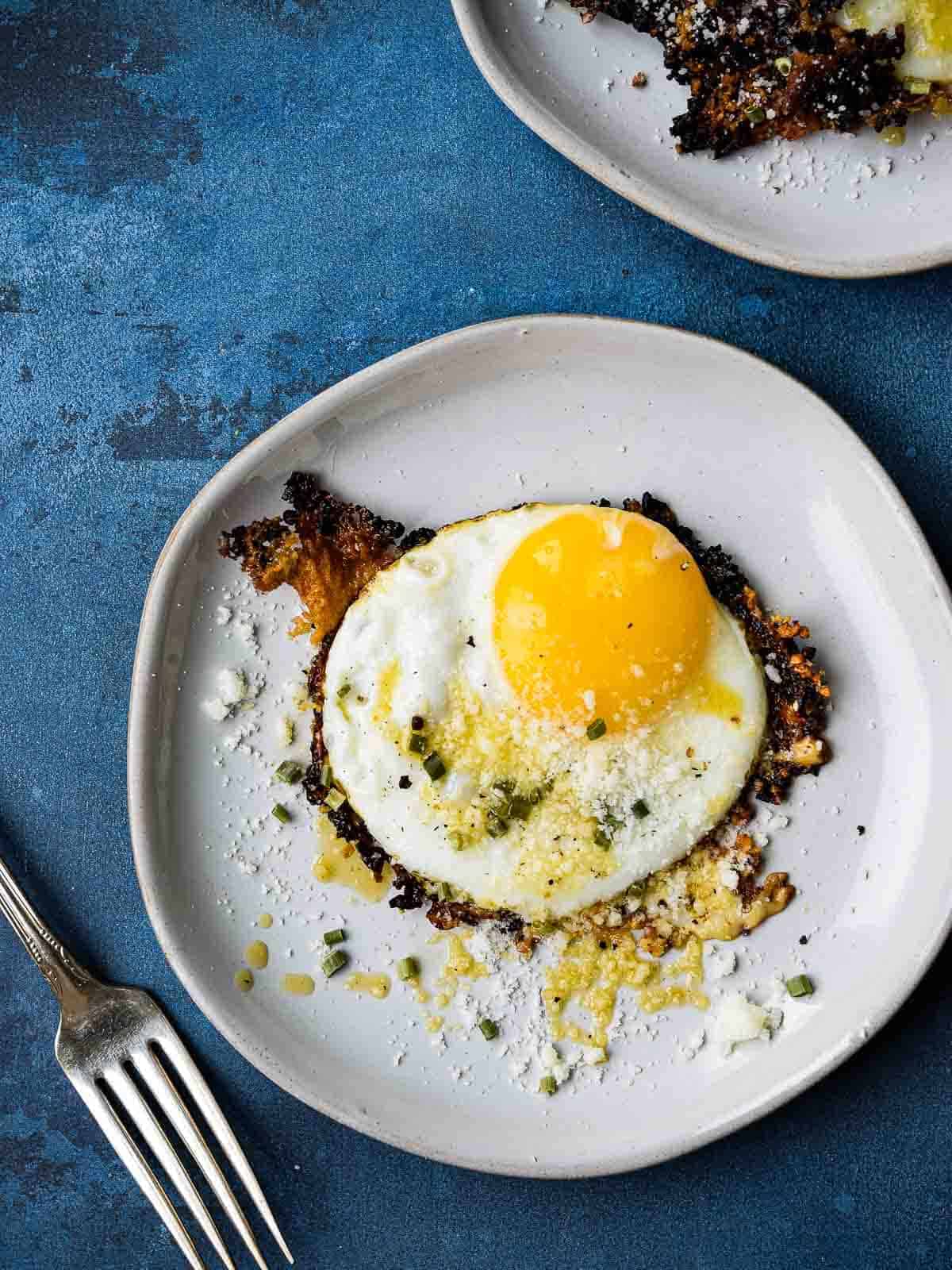 Overhead picture of a fried egg on a white plate, on top of a blue background.