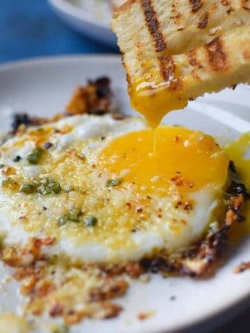 Fried egg with bread being dunked in a runny yolk.