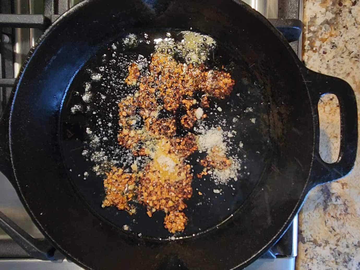 Chili crisp and parmesan cheese added to a hot skillet.
