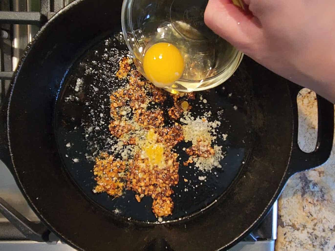 An egg is poured into a hot skillet for frying with spices.