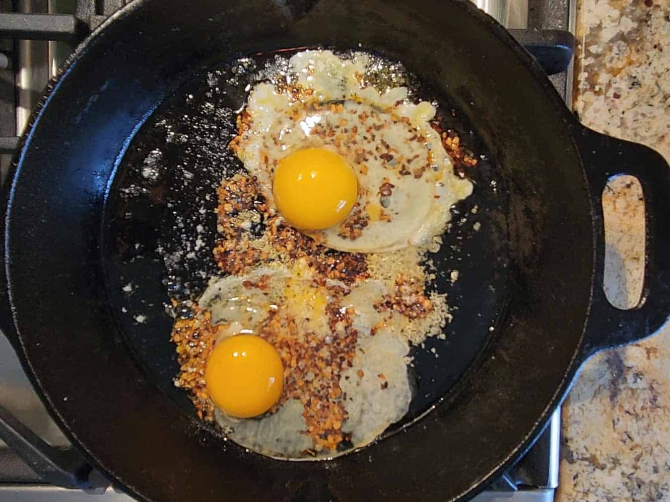 Two eggs frying in a hot skillet with spices.