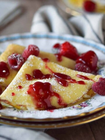 Close-up of ricotta and lemon stuffed crepes with a raspberry sauce on top.