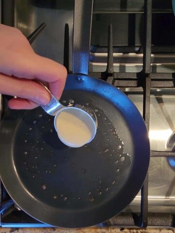 Pouring crepe batter into a hot buttered skillet.