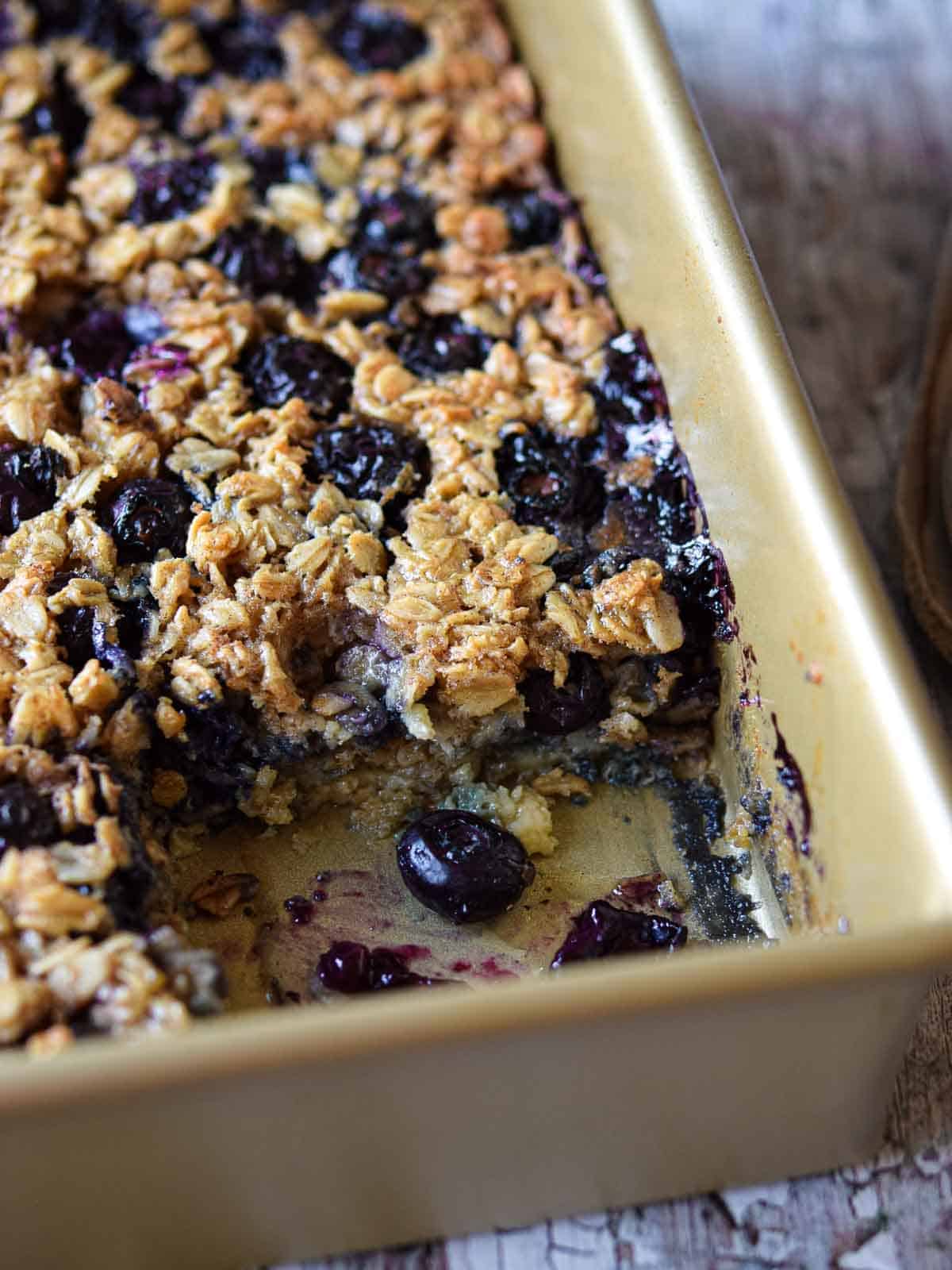 Baked blueberry oatmeal in a baking pan with a slice cut out.