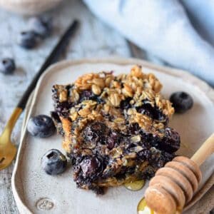A slice of blueberry baked oatmeal on a plate with blueberries.