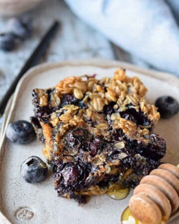 A slice of blueberry baked oatmeal on a plate with blueberries.