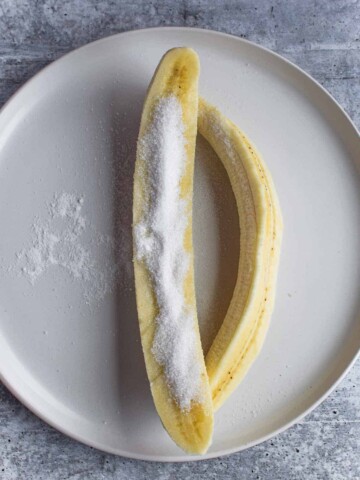 Sliced banana on a white plate with sugar on it.