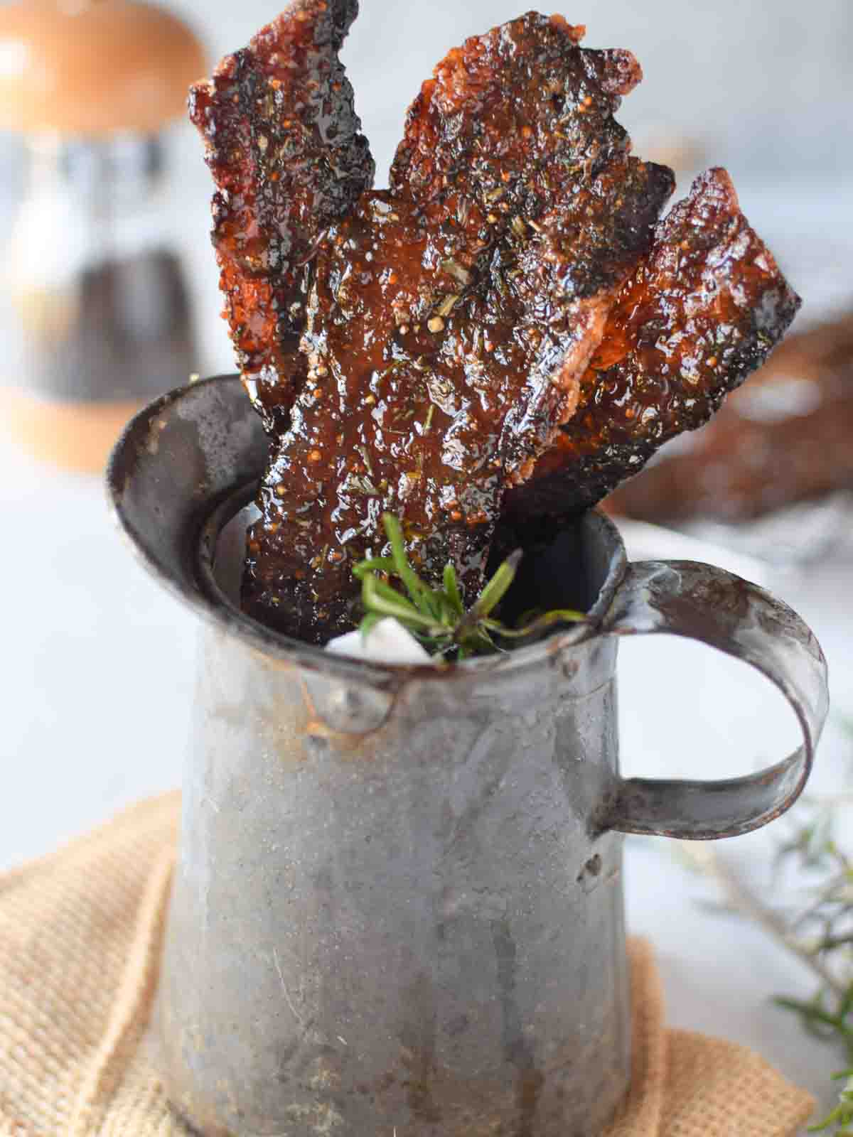 Candied bacon with rosemary and fig in a metal serving pitcher.